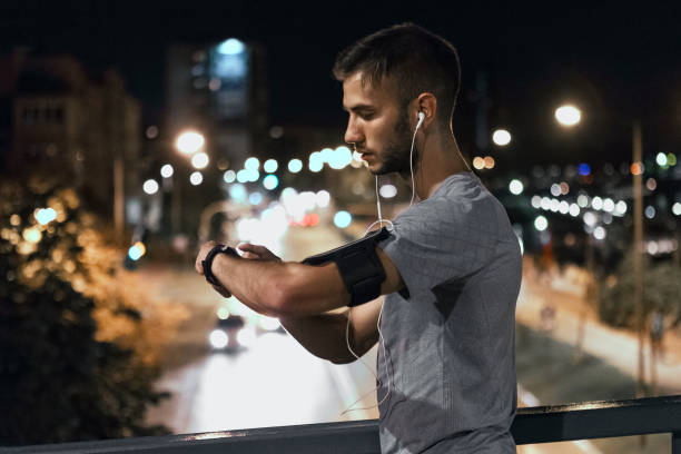 istock Young man jogging through the city at night ,adjusting smart watch 1026556256