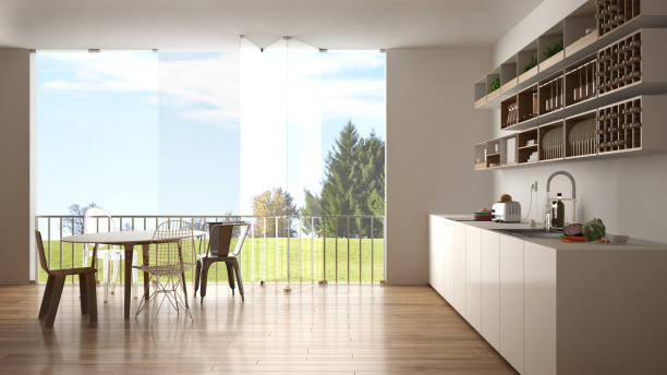 istock Minimalist white and wooden kitchen with dining table and big panoramic window. Meadow with green grass, trees and blue sky in the background. Eco house interior design 1026571982