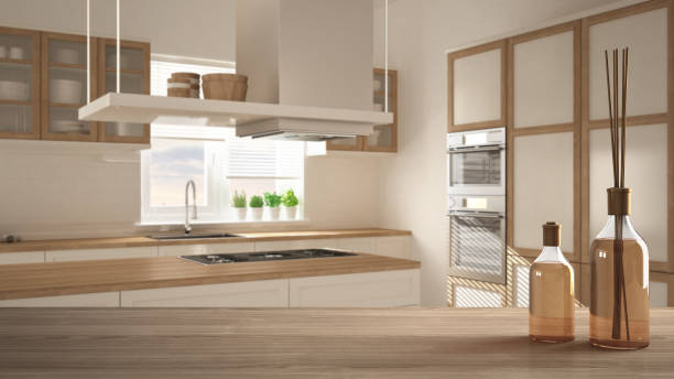 istock Wooden table top or shelf with aromatic sticks bottles over blurred modern kitchen with island, white architecture interior design 1026572458