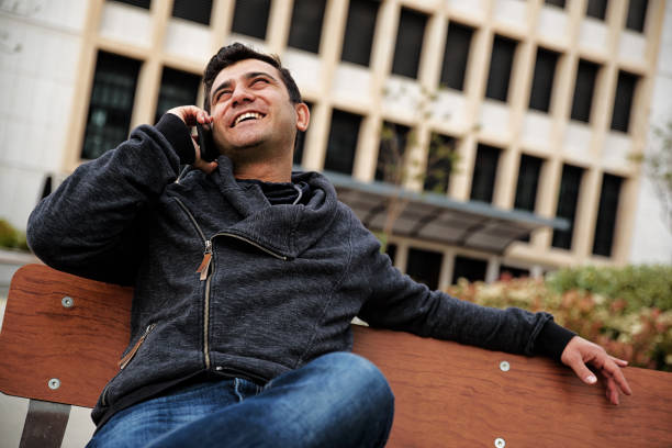 istock Young man on bench with talking mobile phone 1026594128