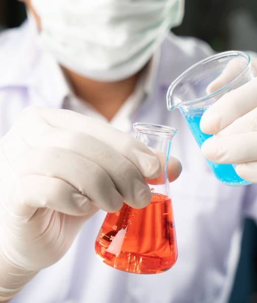 chemiker student junge blaue flüssigkeit beger glas erlenmeyerkolben chemie mit roter flüssigkeit auf biochemischen experiment in gießen. mix-wasser im labor. - gasohol stock-fotos und bilder