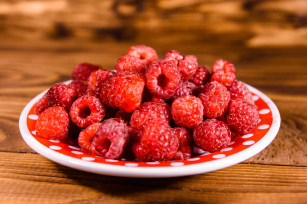 istock Ceramic plate with ripe raspberries on wooden table 1026607016