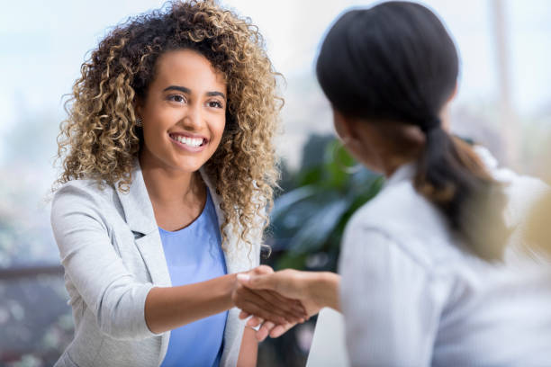 Young woman enjoys meeting new therapist A beautiful young woman smiles and shakes hands with her new unrecognizable therapist. social grace stock pictures, royalty-free photos & images