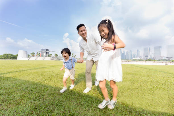 Single dad plays with young daughter and son in a city park. They are running while holding hands.