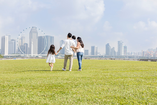 Young family walks in a green field with a city skyline in the background.