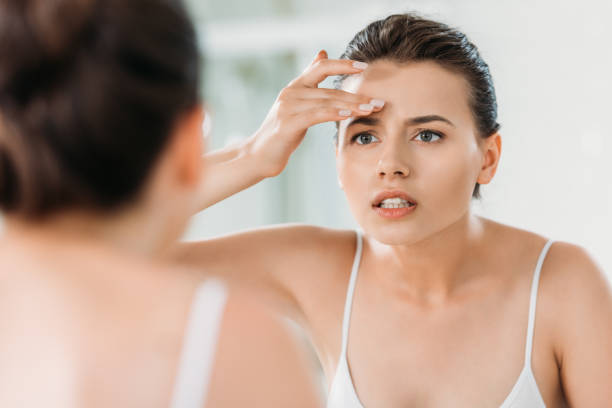 istock attractive young woman touching forehead and looking at mirror in bathroom 1026612108