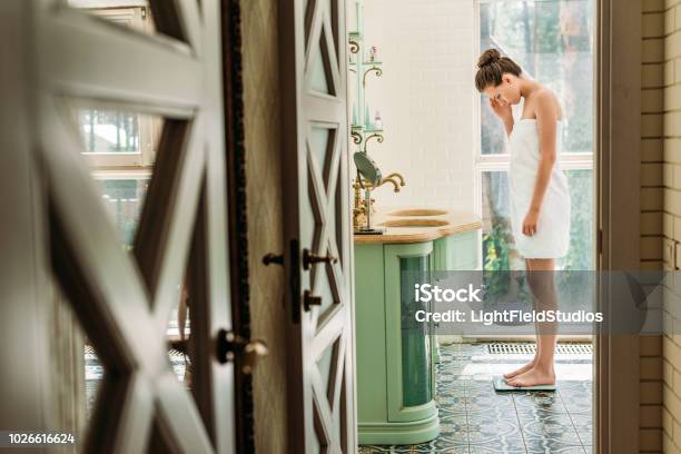 Beautiful Upset Woman In Towel Standing On Digital Scales In Bathroom Stock Photo - Download Image Now