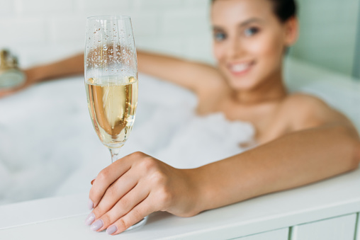 close-up view of beautiful smiling young woman holding glass of champagne in bathtub