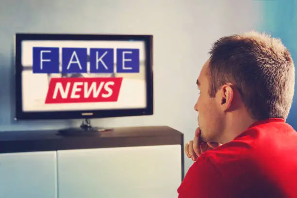 Photo of lies of tv propaganda mainstream media disinformation, A fake news report. viewer is watching TV and doesn't believe in fake news. man closes his eyes not to watch the lies on TV.