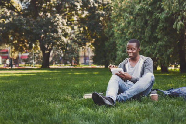 istock Happy african-american studen sitting with notebook on grass 1026617338