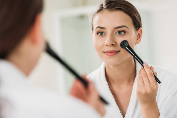 istock smiling young woman looking at mirror and applying makeup in bathroom 1026617476