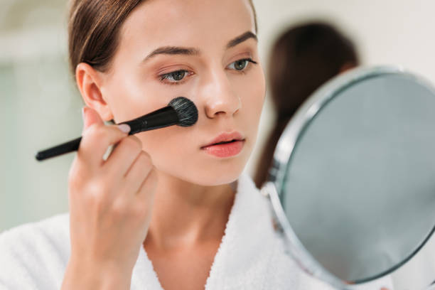 istock beautiful young woman in bathrobe applying makeup and looking at mirror 1026617538