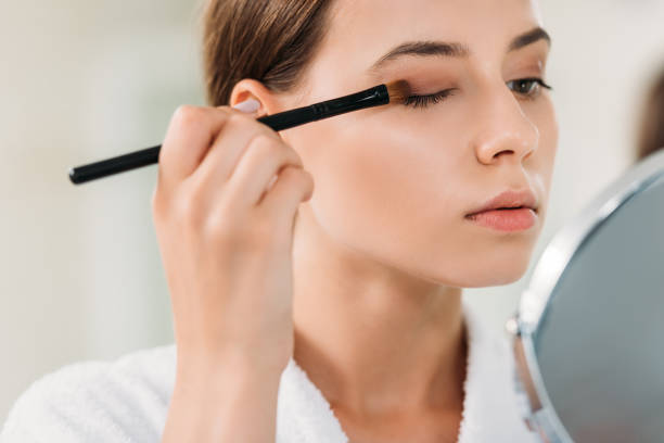 vista ravvicinata di bella giovane donna applicando ombretto con pennello - trucco per gli occhi foto e immagini stock