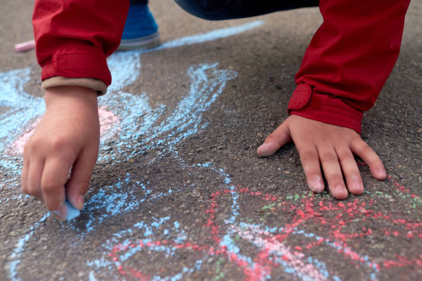 istock Hands of unrecognizable preschool boy drawing on asphalt with red and blue chalks 1026623318