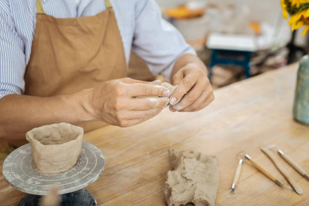 istock Ceramist wearing apron sitting at the table forming little items 1026627556