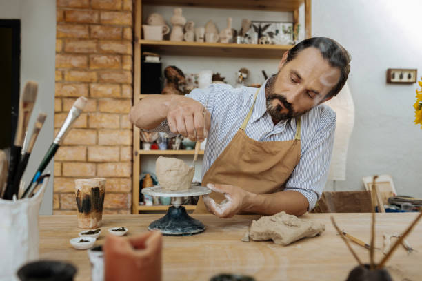 istock Dark-haired potter forming little pots using pottery wheel 1026631538