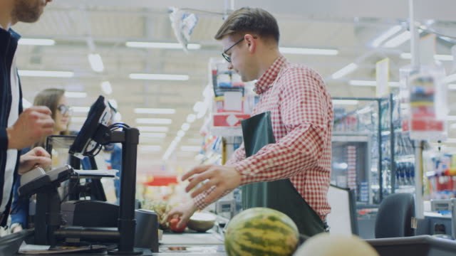 At the Supermarket: Checkout Counter Happy Customer Chats with Friendly Cashier who Scans Fresh Groceries and Fruits. Modern  Shopping Mall with Wireless Paying Terminal System.