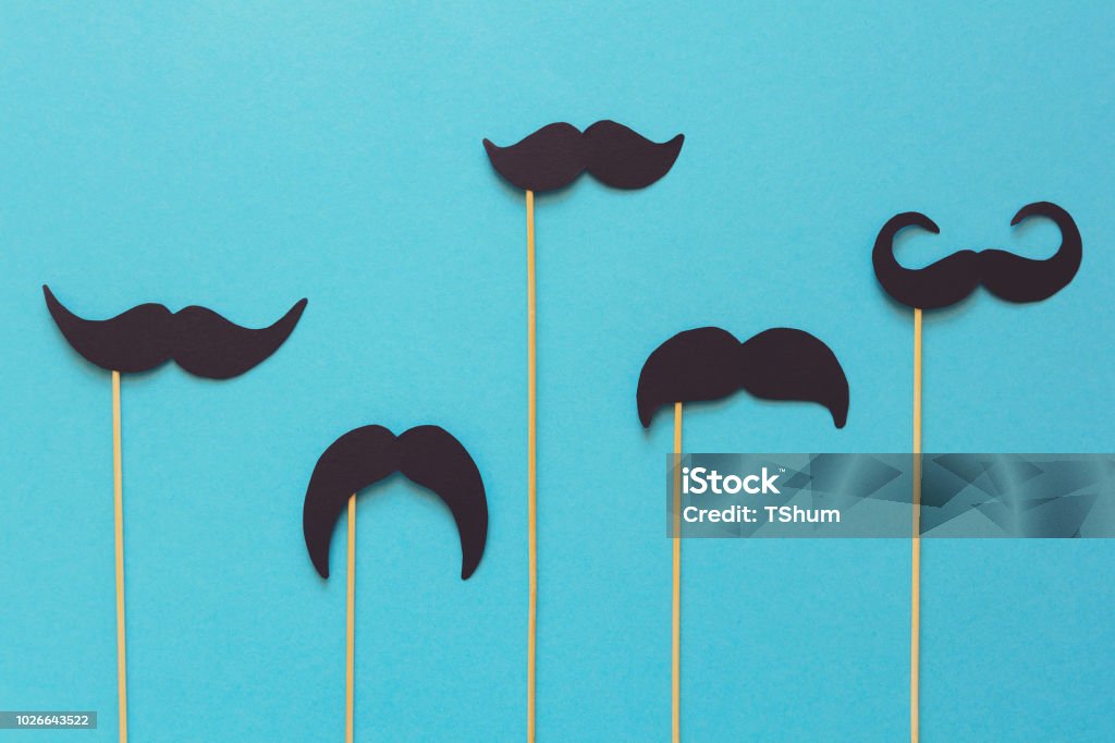 Papier-Schnurrbart auf Stand Requisiten auf blauem Papierhintergrund. Schneiden Sie Stil. Movember oder Mann Gesundheitskonzept. Ansicht von oben. Flach zu legen. Kopieren Sie Raum. Getönten - Lizenzfrei Movember Stock-Foto