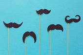 Paper mustache on booth props on blue paper background. Cut out style. Movember  or man health concept. Top view. Flat lay. Copy space. Toned