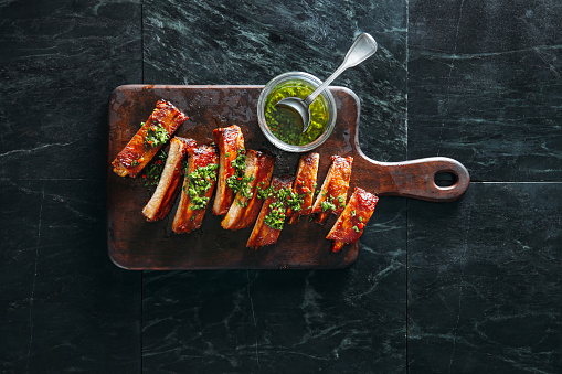 Grilled pork ribs with chimichurri and herbs on dark background