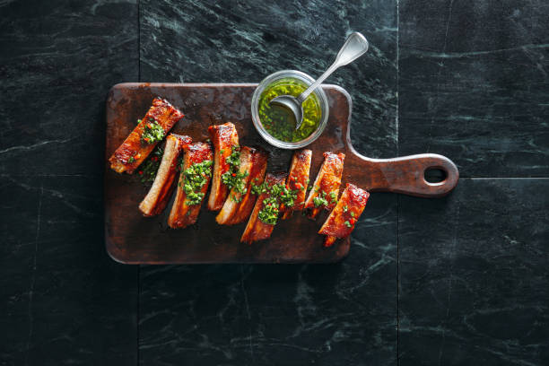 Bbq pork ribs Grilled pork ribs with chimichurri and herbs on dark background barbecue pork stock pictures, royalty-free photos & images