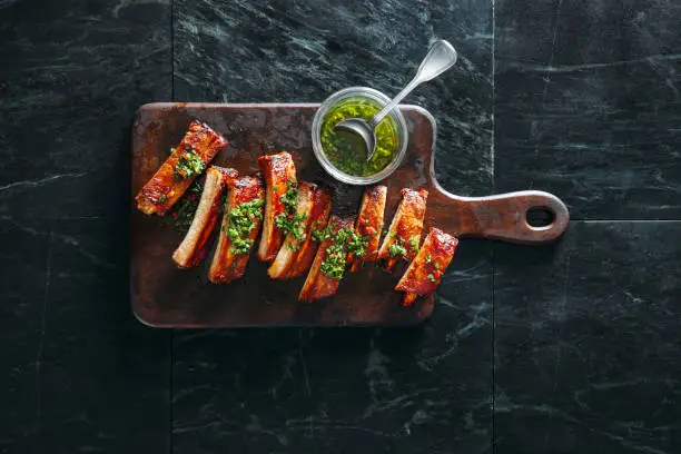 Grilled pork ribs with chimichurri and herbs on dark background