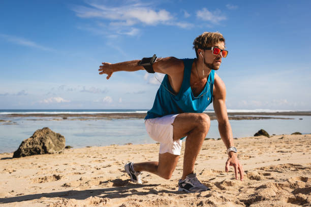 istock sportive man with armband doing lunges during workout on beach near sea 1026653500