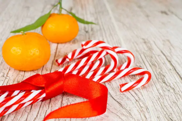 christmas candy cane with red ribbon and tangerines on white rustic table
