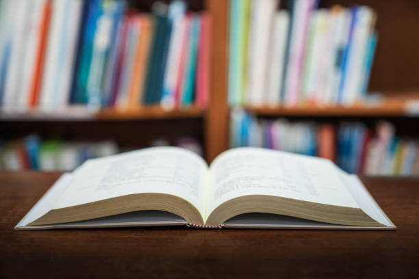 istock Education learning concept with opening book or textbook in old library, stack piles of literature text academic archive on reading desk and aisle of bookshelves in school study class room background 1026671734