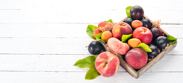 Fresh fruits in a wooden box. Apricot, peach, nectarine, plum. On a wooden background. Top view. Free space for your text.