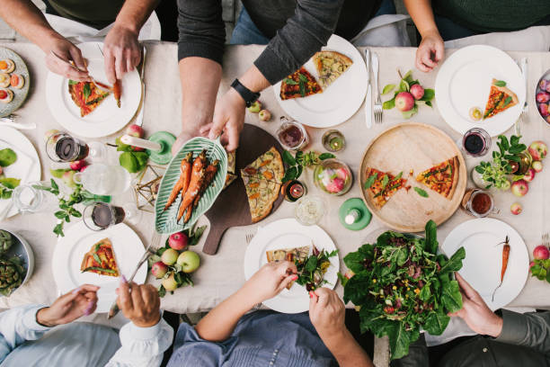Friends enjoying a dinner together in greenhouse harvest party Friends enjoying a dinner together in greenhouse harvest party
photo of group of people eating, photo taken overhead table top shot vegan food photos stock pictures, royalty-free photos & images