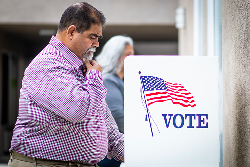 A senior mexican man at the voting booth holding his I voted sticker