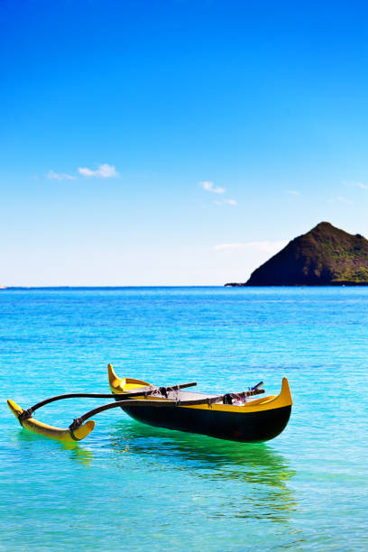 Outrigger Canoe off Lanikai Beach with Mokulua Island, Oahu, Hawaii The outrigger canoe, a local boat vessel in the Hawaiian culture with the Mokulua Island in the background, photographed on Lanikai Beach of Oahu, Hawaii. outrigger stock pictures, royalty-free photos & images