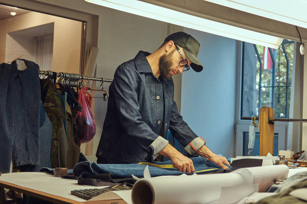 istock Handsome bearded tailor makes measurements of jeans cloth samples at sewing workshop. 1026699008