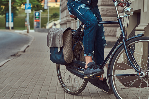 Cropped image of a fashionable man in stylish clothes riding on city bicycle.