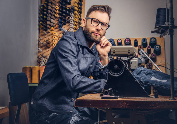istock Pensive tailor sitting at a table with hand on chin in a sewing workshop. 1026704652