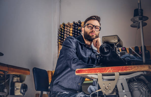 istock Pensive tailor sitting at a table with hand on chin in a sewing workshop. 1026704884