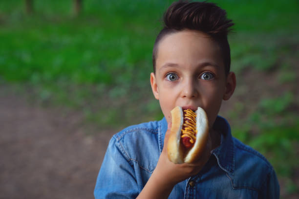 a young boy takes a bite of a hot dog stock photo