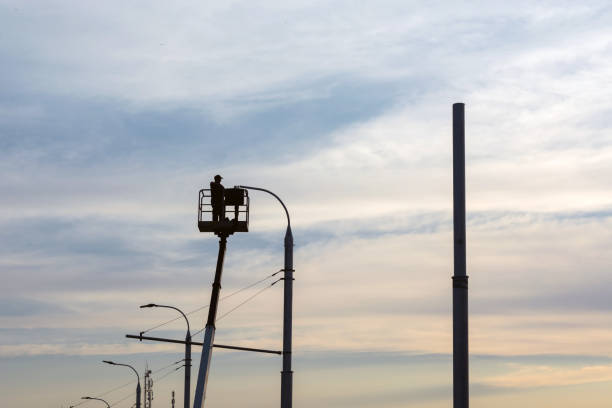 an electrician man sets a lantern on a pole, against the sky, during sunset