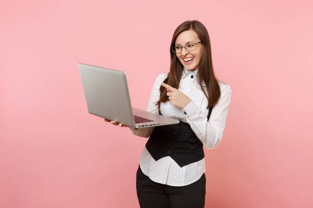 istock Young laughing attractive business woman holding using laptop pc computer pointing index finger isolated on pink background. Lady boss. Achievement career wealth concept. Copy space for advertisement. 1026717824