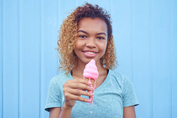 smiling black girl with pink melting ice cream at blue wall background stock photo