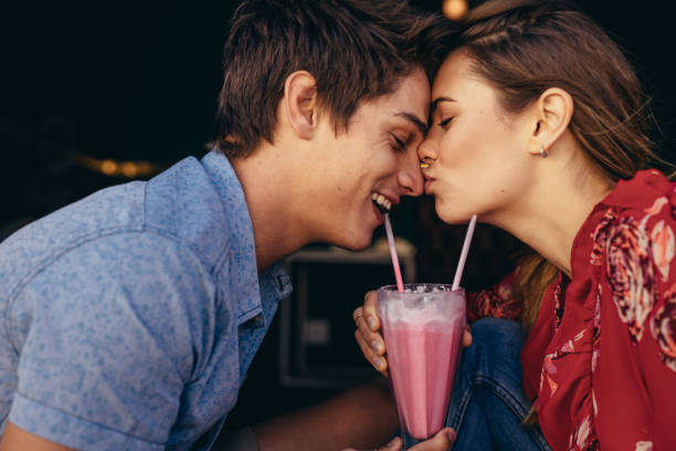 Romantic couple on a date at a restaurant Woman kissing her boyfriend on his nose while on date at a restaurant. Couple at a restaurant in romantic mood sharing a milkshake. kissing stock pictures, royalty-free photos & images
