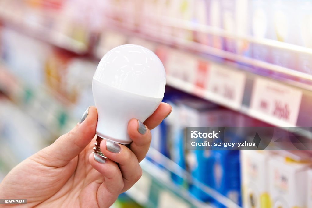 Energisparande LED lampa i händerna på köparen i butik - Royaltyfri Glödlampa Bildbanksbilder