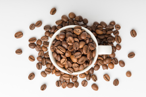 Medium roasted coffee beans in a white espresso cup on white background viewed from above
