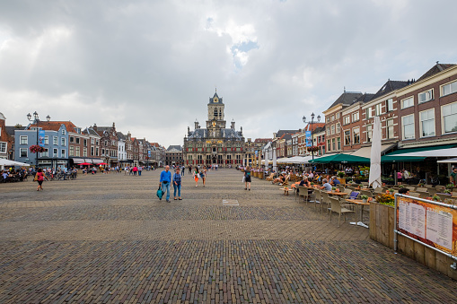 Delft, the Netherlands - Aug 21, 2018 : The market square with the old town hall in the background and restaurants with terraces full of tourists in the city center of Delft, the Netherlands.