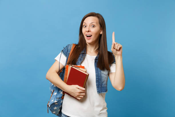 istock Young shocked woman student with backpack pointing index finger up on copy space and got new idea holding school books isolated on blue background. Education in high school university college concept. 1026755372