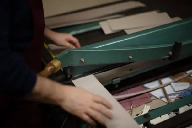 Man cutting paper and card on a large guillotine on a work table in a book binders workshop in a close up view