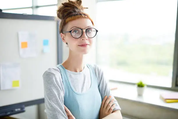 Ambitious confident hipster startupper with short fringe smiling at camera and crossing arms on chest in office