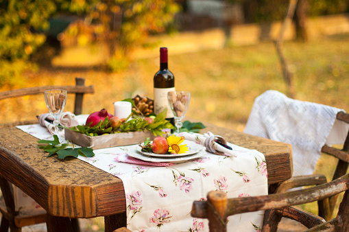 Romantic dinner in the autumn garden, table setting for a nice dinner. Wine, fruit, pomegranate and flowers. Picnic in the open air