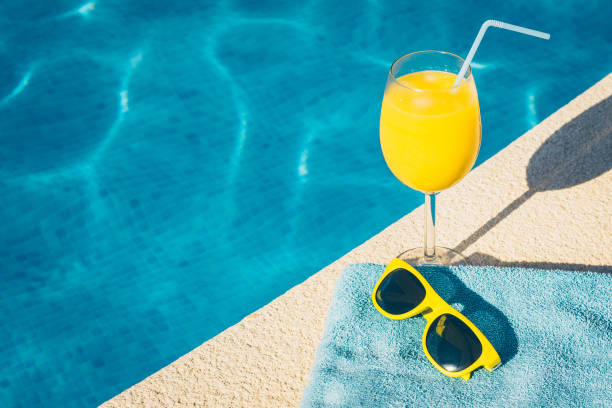 gafas de sol y un vaso de jugo de naranja en el resort hotel - poolside fotografías e imágenes de stock
